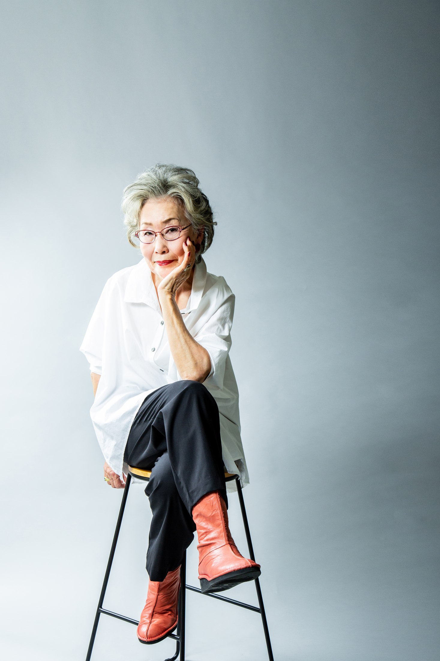 椅子に座り、頬に手を添えてほほ笑む女性