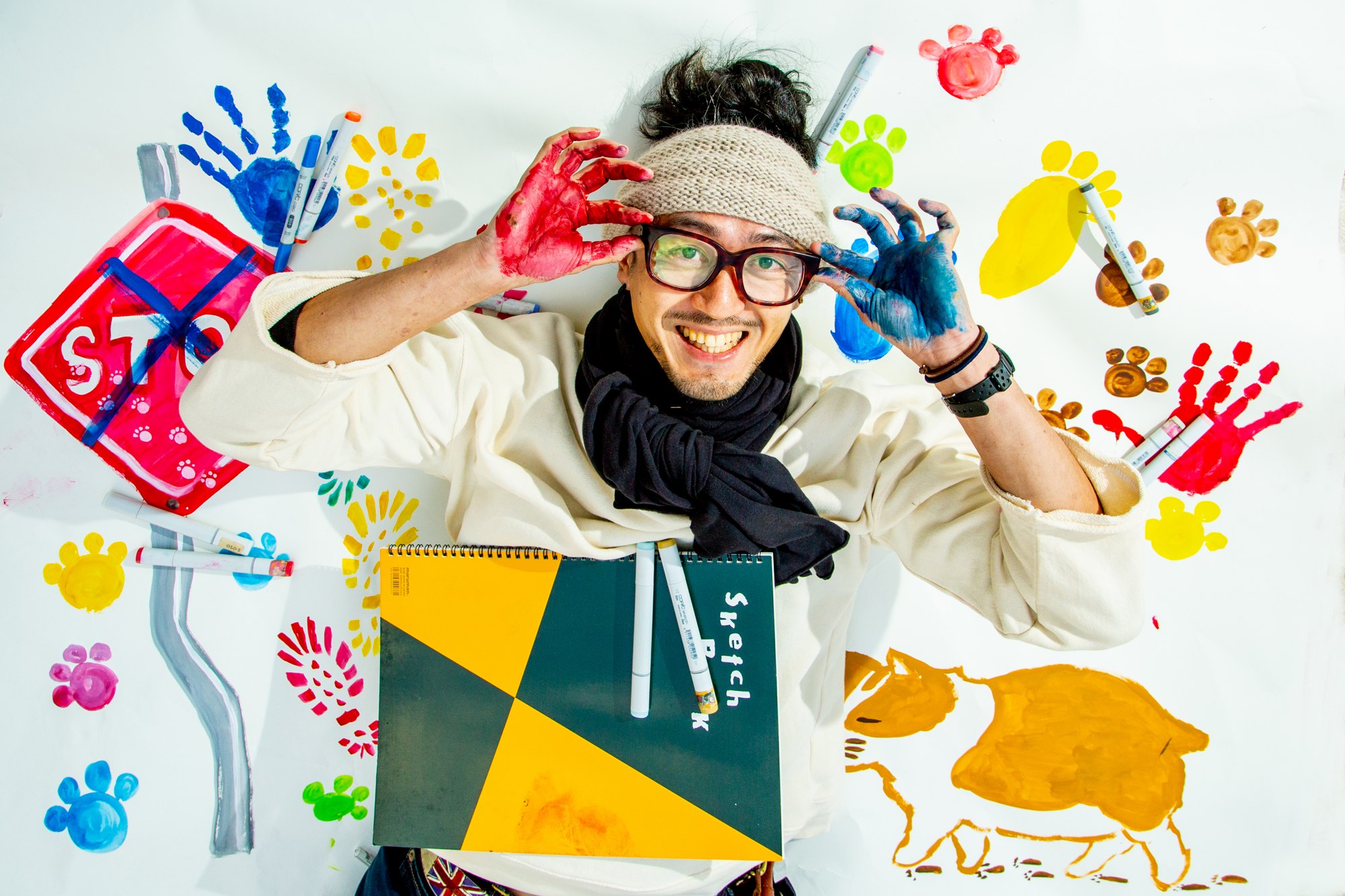 色とりどりの手形を背景に、絵の具のついた手を広げる人物