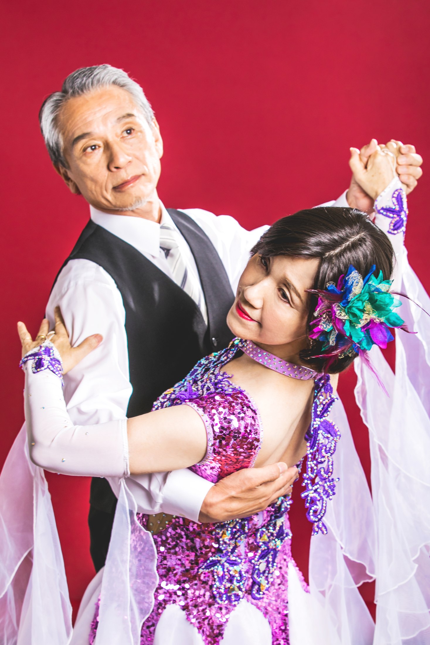 赤い背景の前で、華やかな衣装を着て踊る二人
