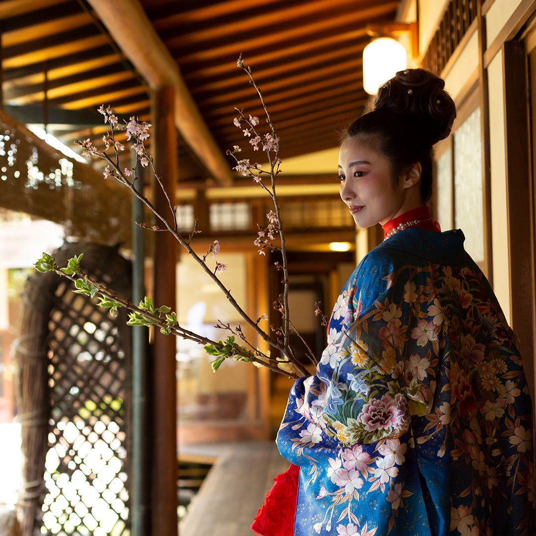 木造の廊下で光を受ける青い着物の女性